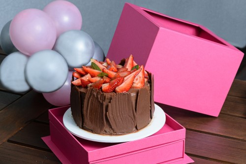 Tort czekoladowy na białym podkładzie w różowym kartonie z okienkiem