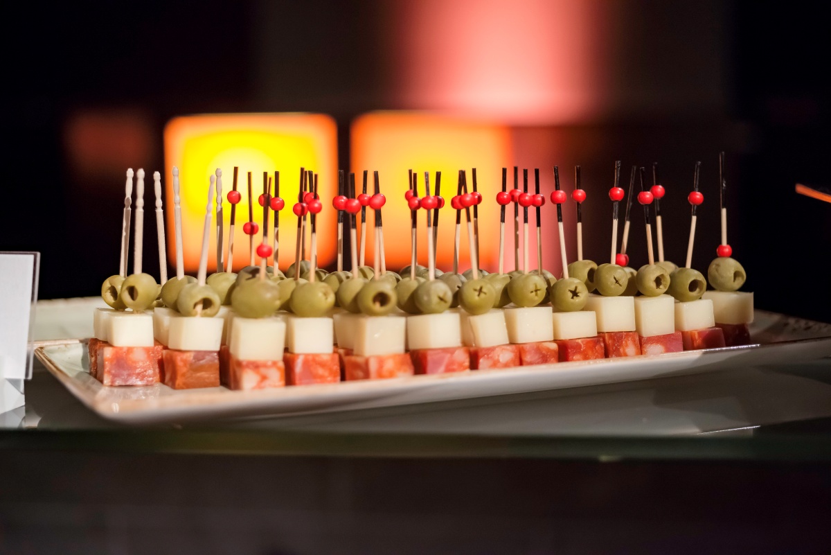 Koreczki z serem, zielonymi oliwkami, salami, na białym półmisku.